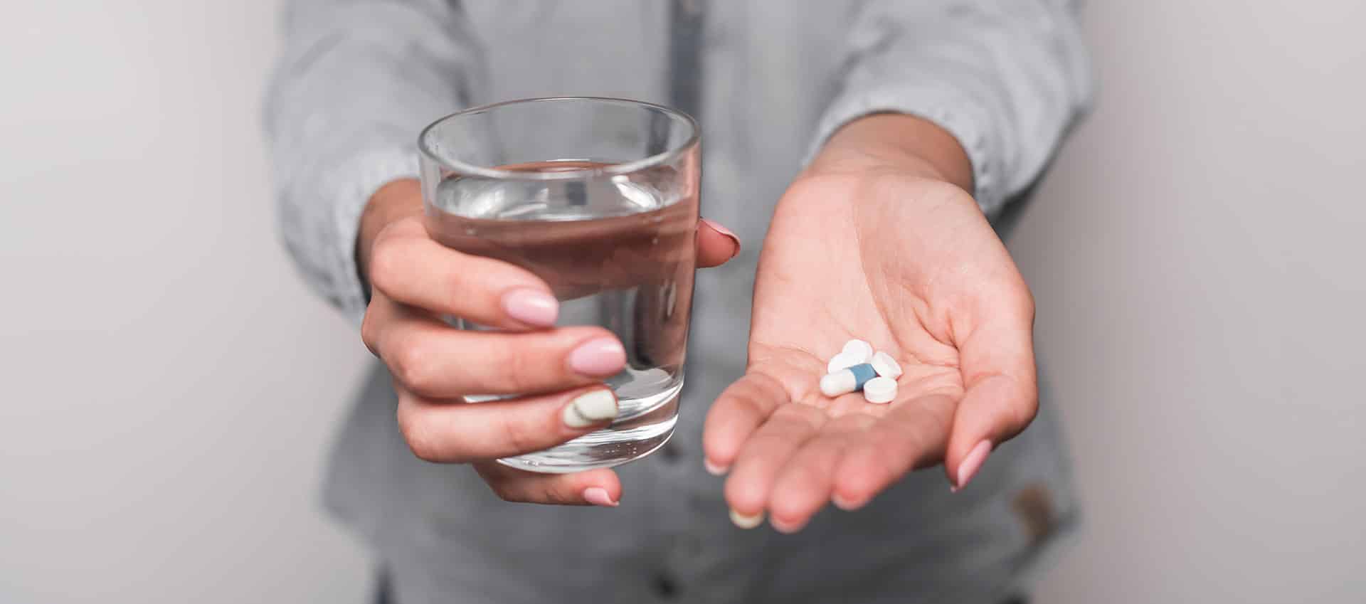 een persoon die een glas vasthoudt met een pil erin.